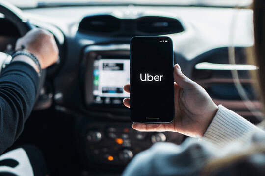 A man is flaunting the Uber app logo on phone in a Uber car.